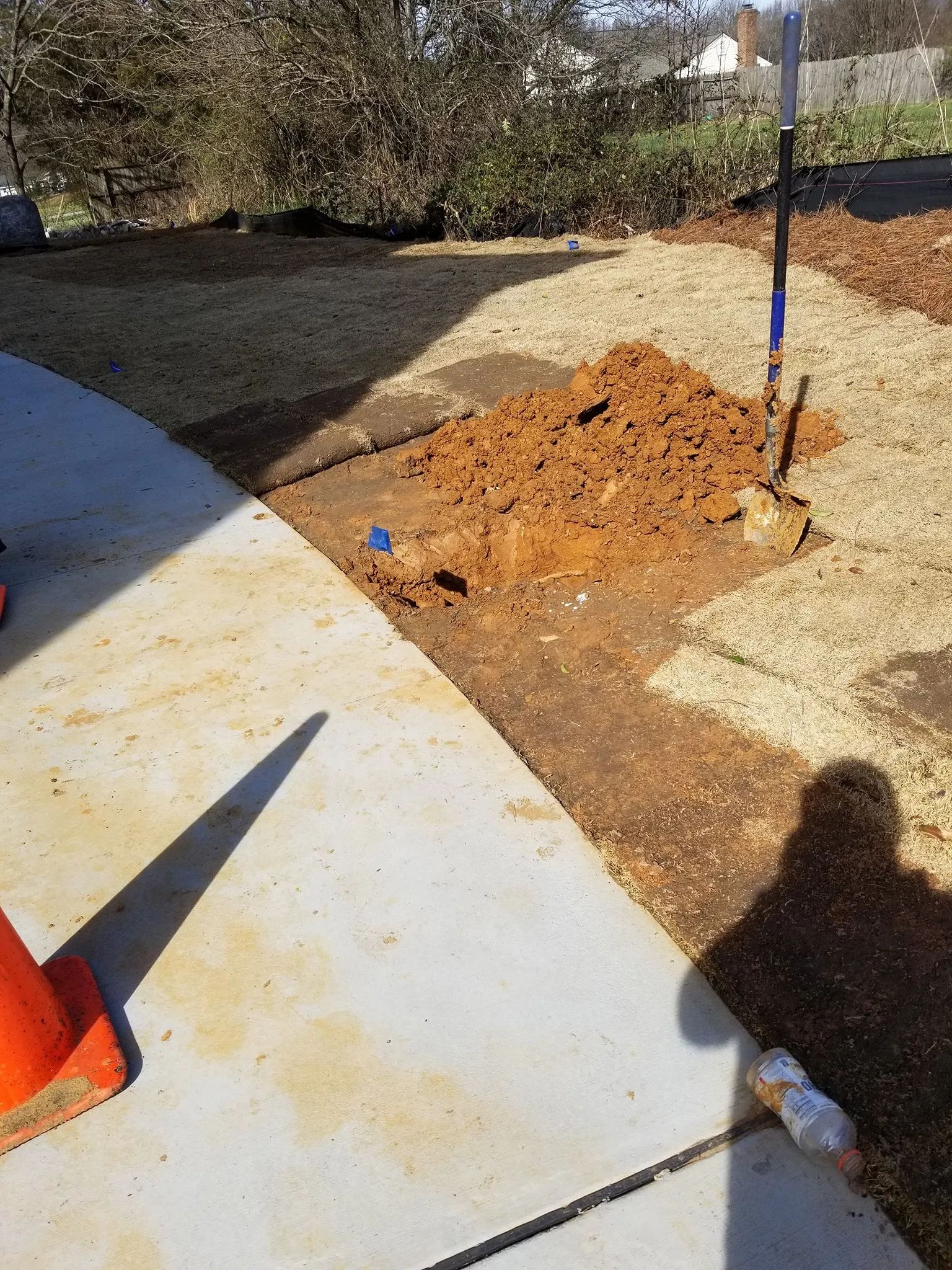 Sidewalk with a dirt pile and shovel on a concrete path in a yard.