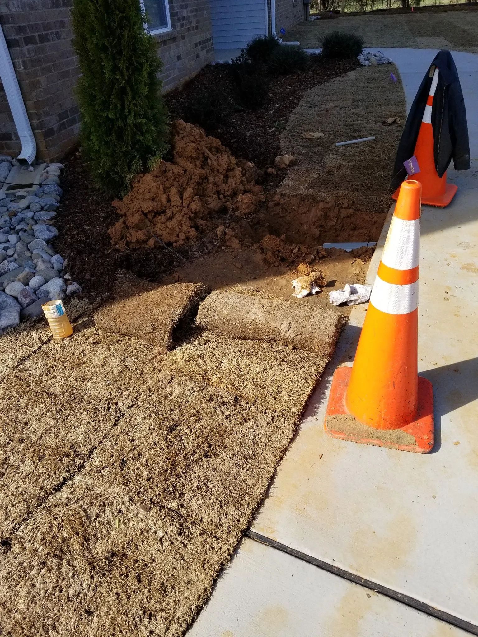 Sidewalk repair area beside a house, with orange traffic cones and exposed dirt near the walkway.