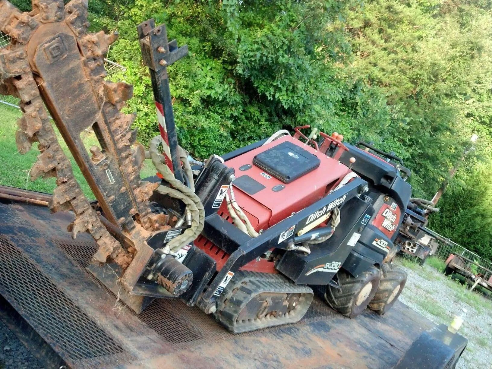 Red excavator climbing a steep dirt slope beside a road in a wooded area