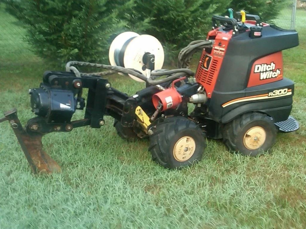 Red and black riding mower attached to a front blade, parked on grass with a hose reel behind it