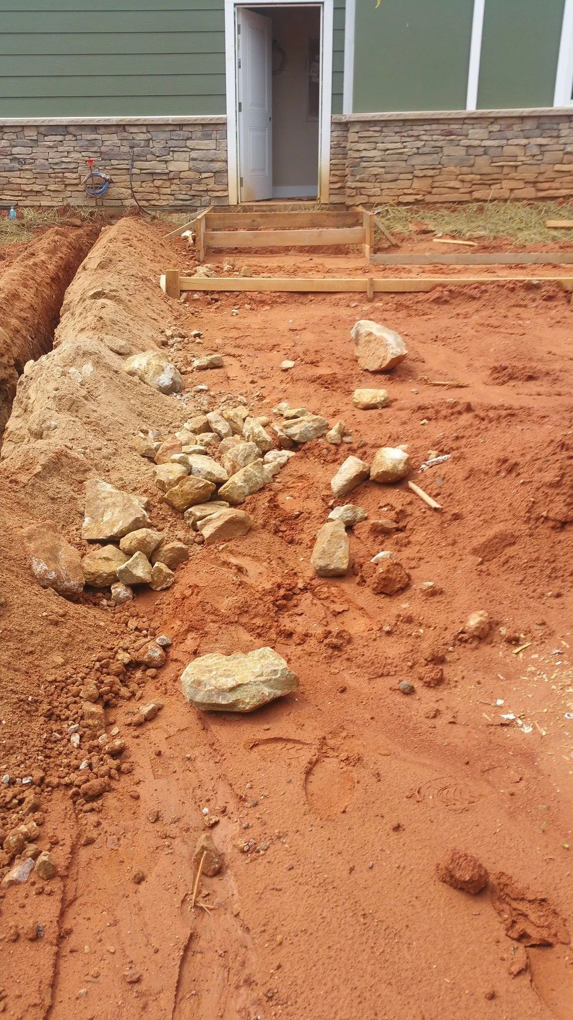 Rough dirt mound and scattered rocks blocking a building entrance with steps and doorway behind