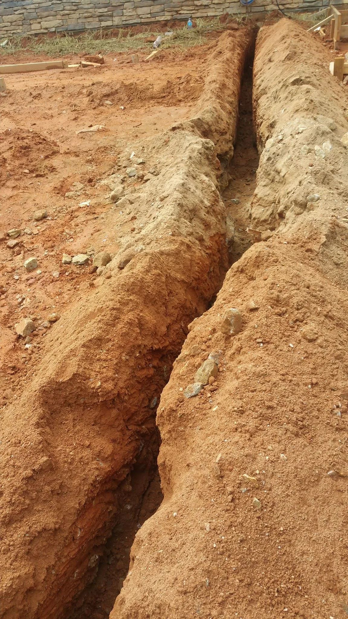 Dirt trench cut into dry, reddish-brown soil at an excavation site.
