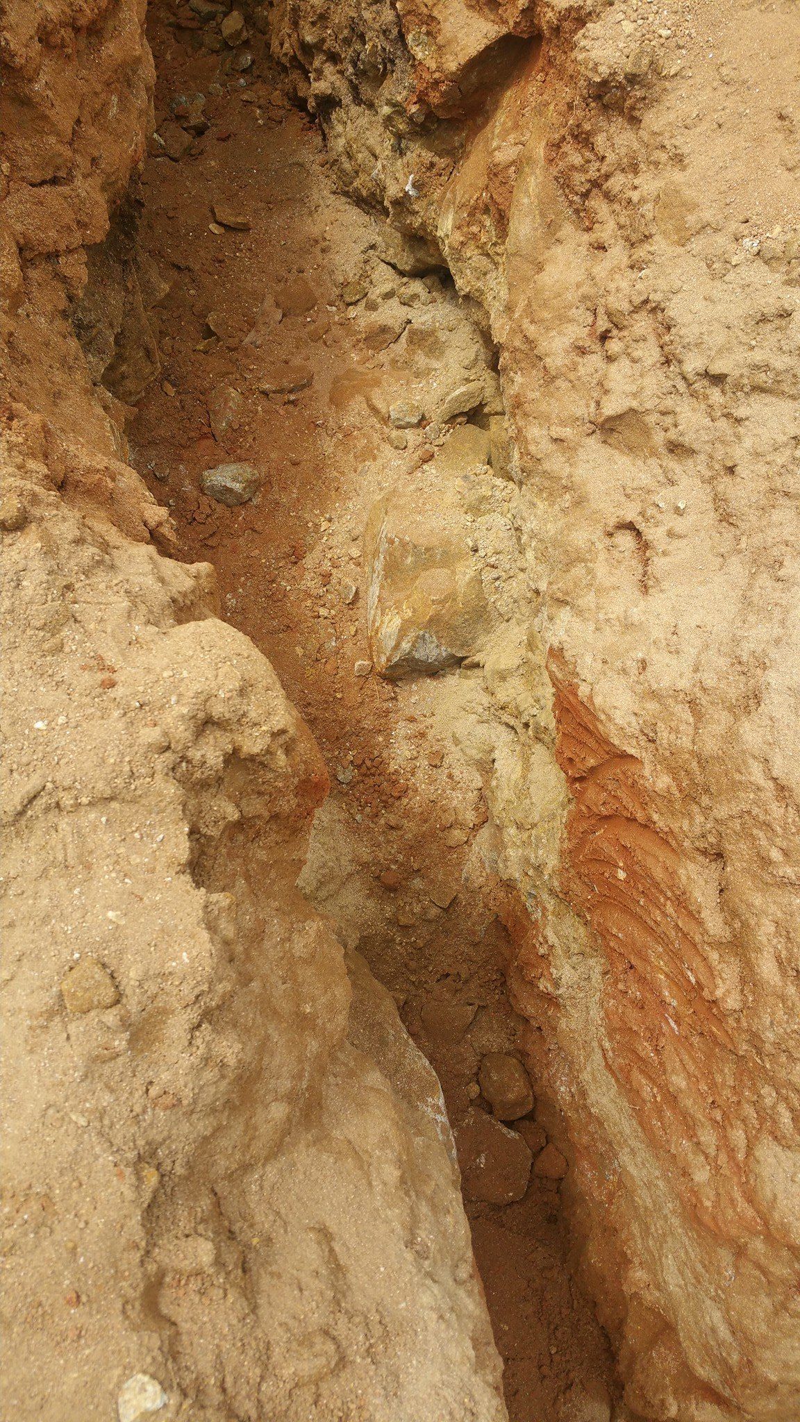Narrow muddy earthen trench with exposed soil walls and a small cracked section near the center