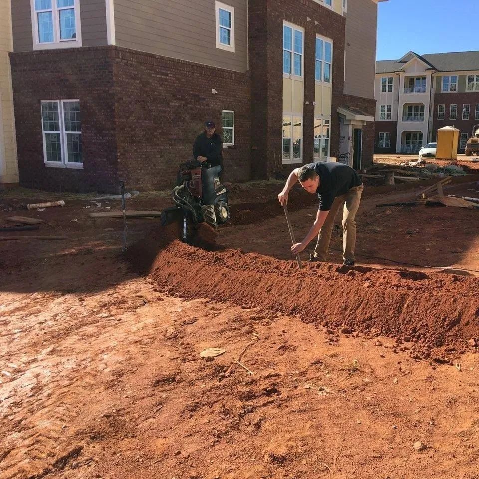 Two workers grading red dirt at a new townhouse construction site