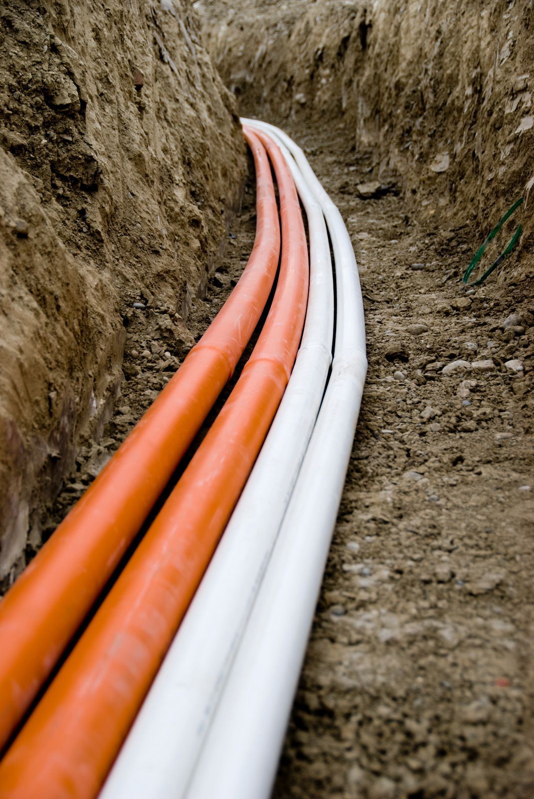 Orange and white utility pipes laid in a trench along a dirt excavation site