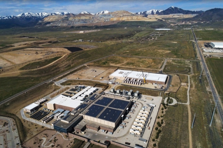 Aerial view of a data center complex in a desert landscape with mountains in the background.