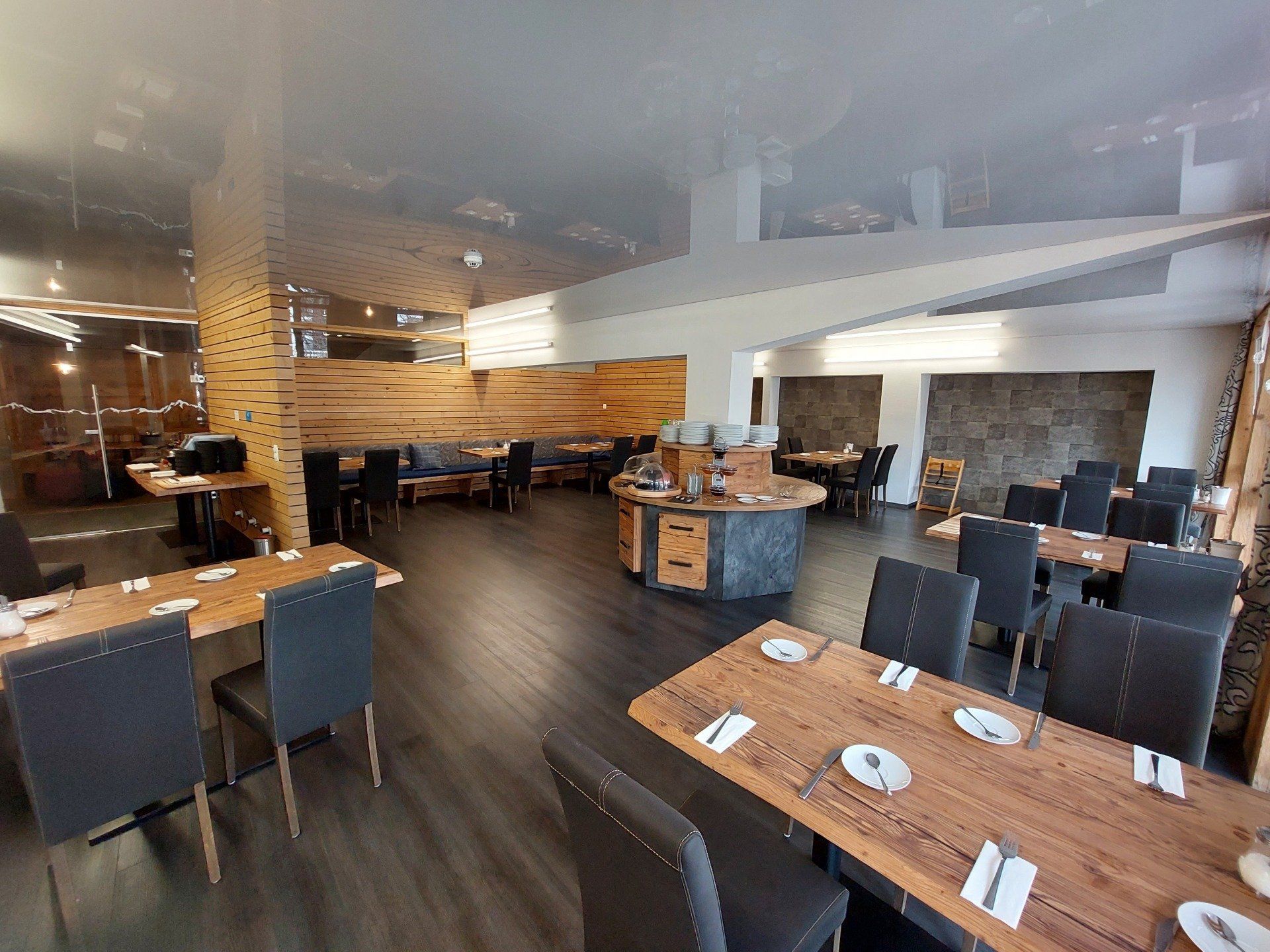 Empty modern restaurant dining room with wooden tables, dark chairs, and warm lighting
