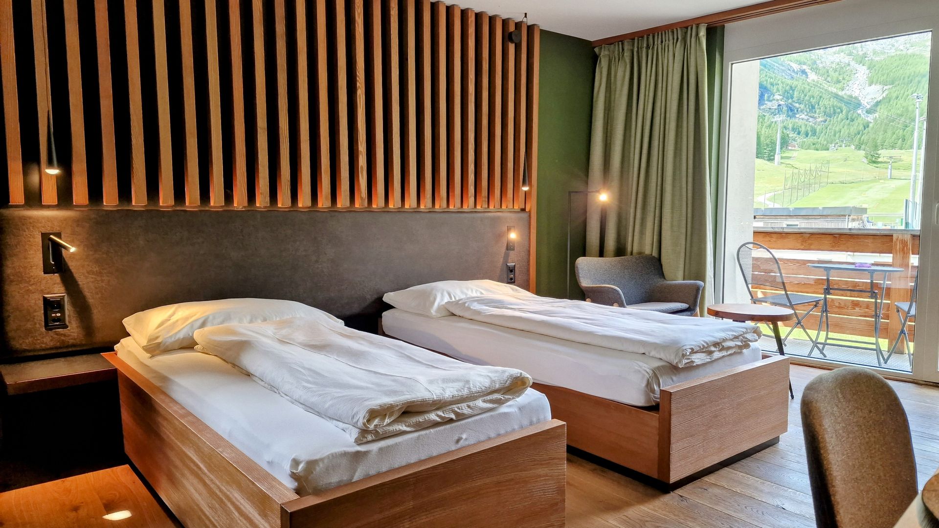Modern hotel room with two beds, wood slat accent wall, and large window overlooking greenery