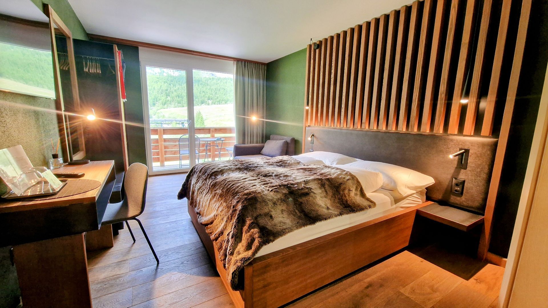 Modern hotel room with a bed, desk, wall lamp, and balcony view through sliding glass doors