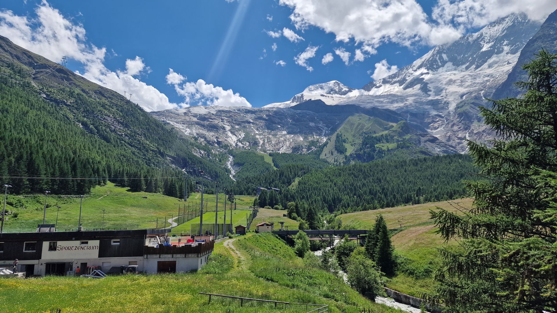 Mountain valley with snow-capped peaks, blue sky, green meadows, and a small village in the foreground