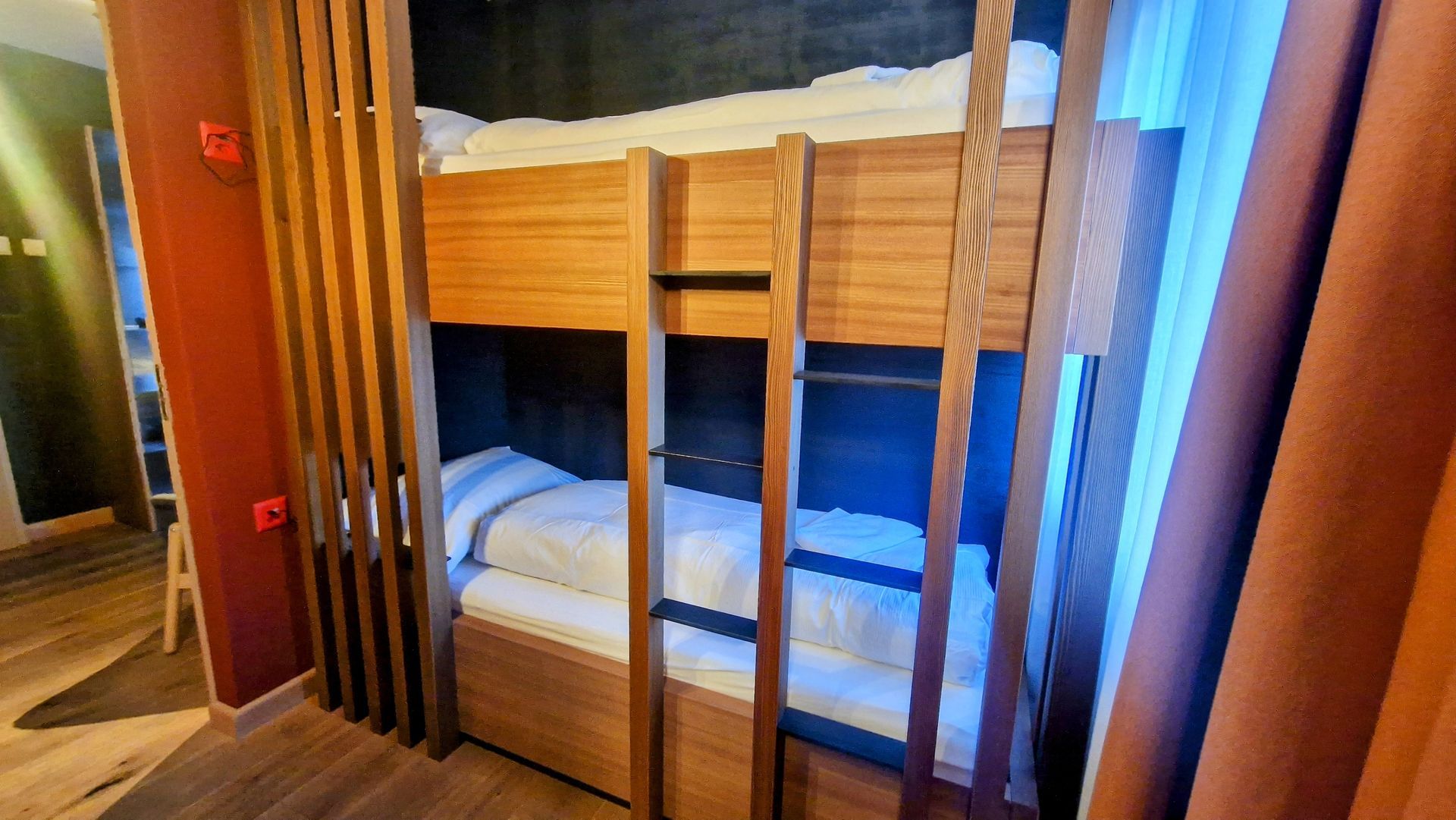 Wooden bunk beds in a compact cabin-style room with a ladder and curtains