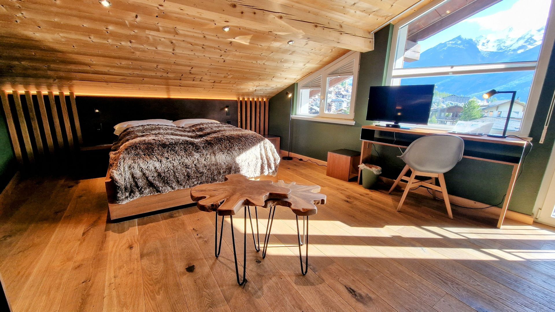 Cozy loft bedroom with sloped wooden ceiling, bed, desk, chair, and large mountain-view windows