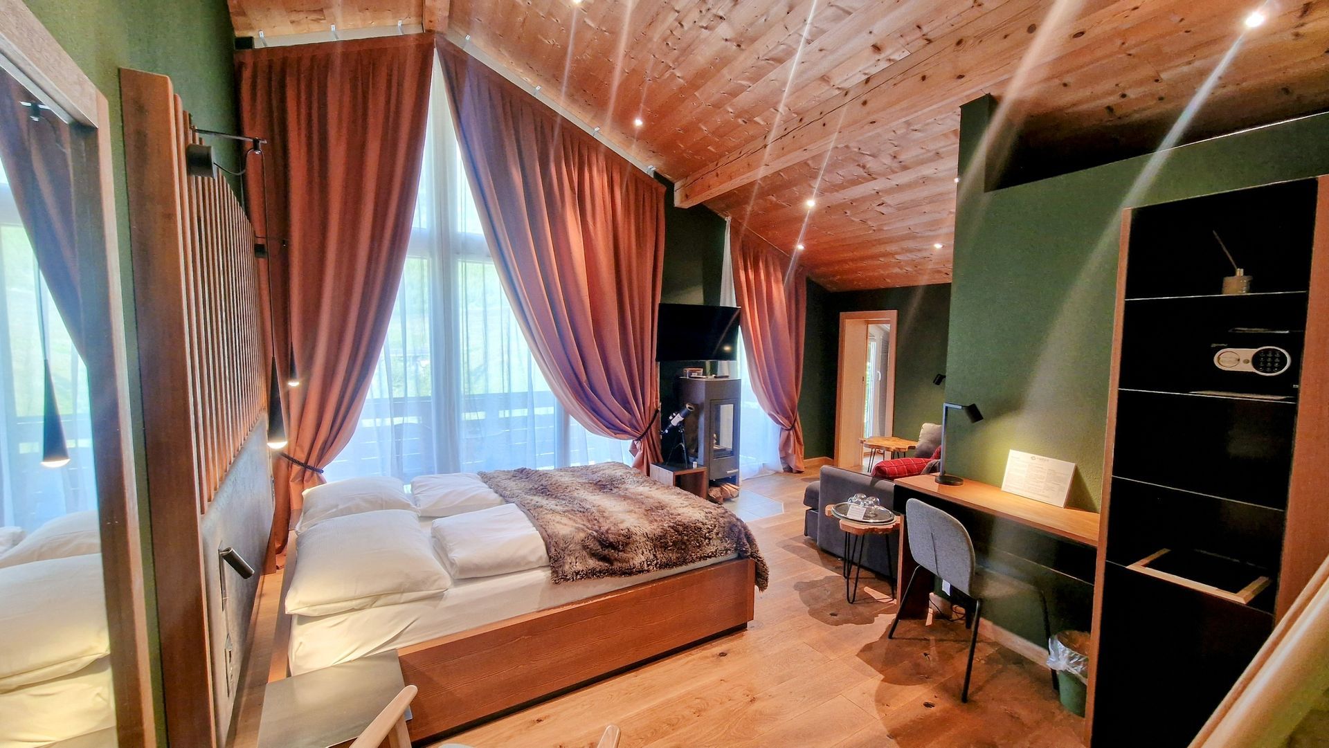 Cozy bedroom with wood ceiling, green walls, draped windows, bed, desk, and open shelving with warm lamp light