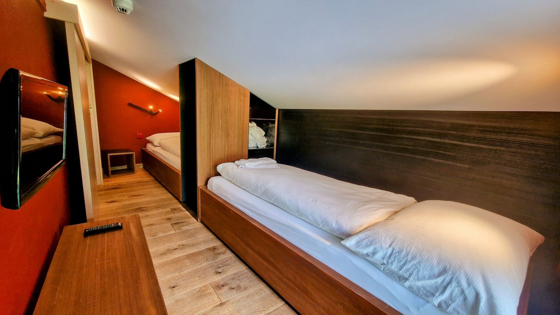 Modern hotel room with a bed, wood-paneled wall, orange accent wall, and hallway view