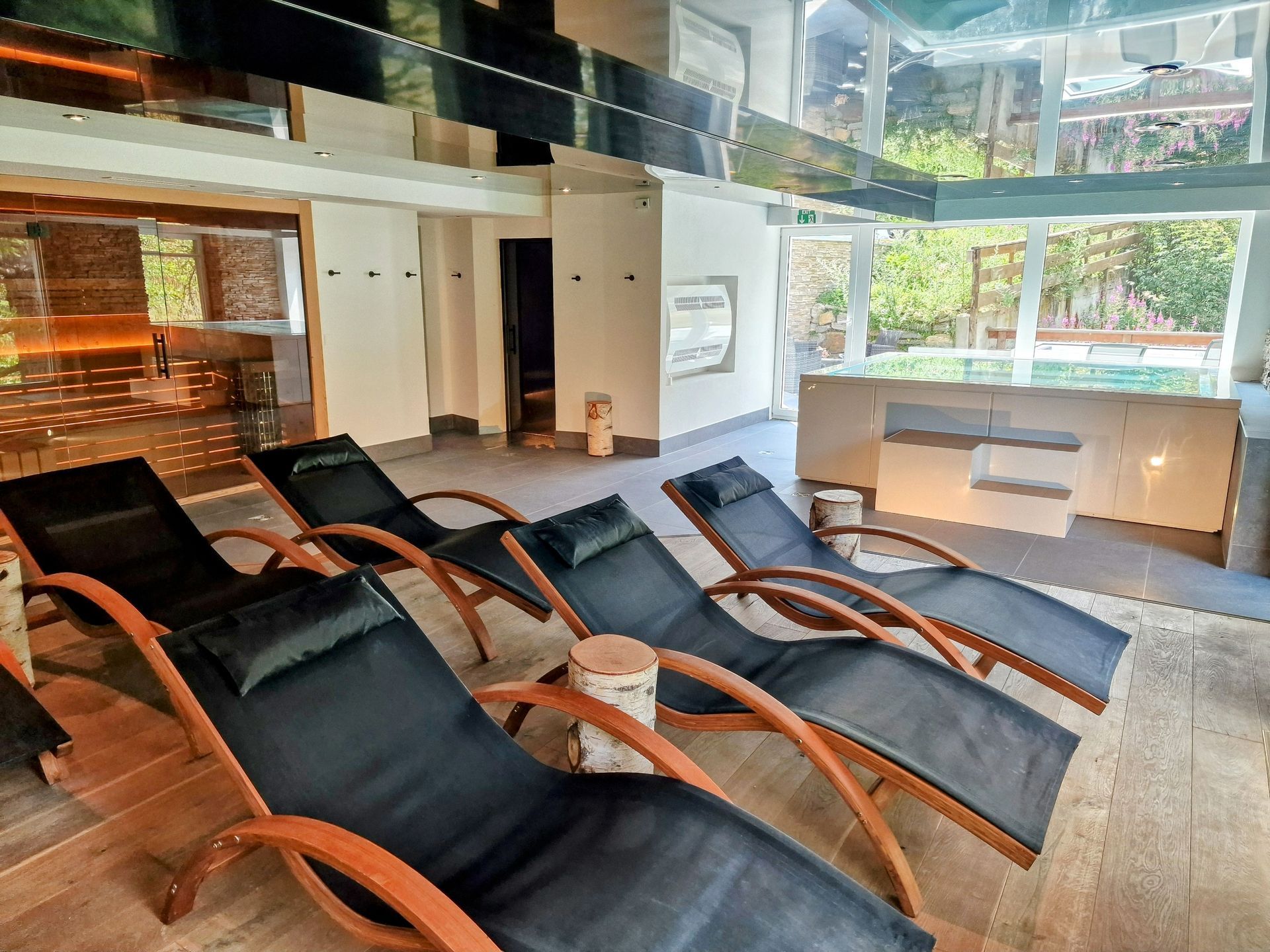 Modern spa lounge with black reclining chairs, wood armrests, and large windows overlooking greenery