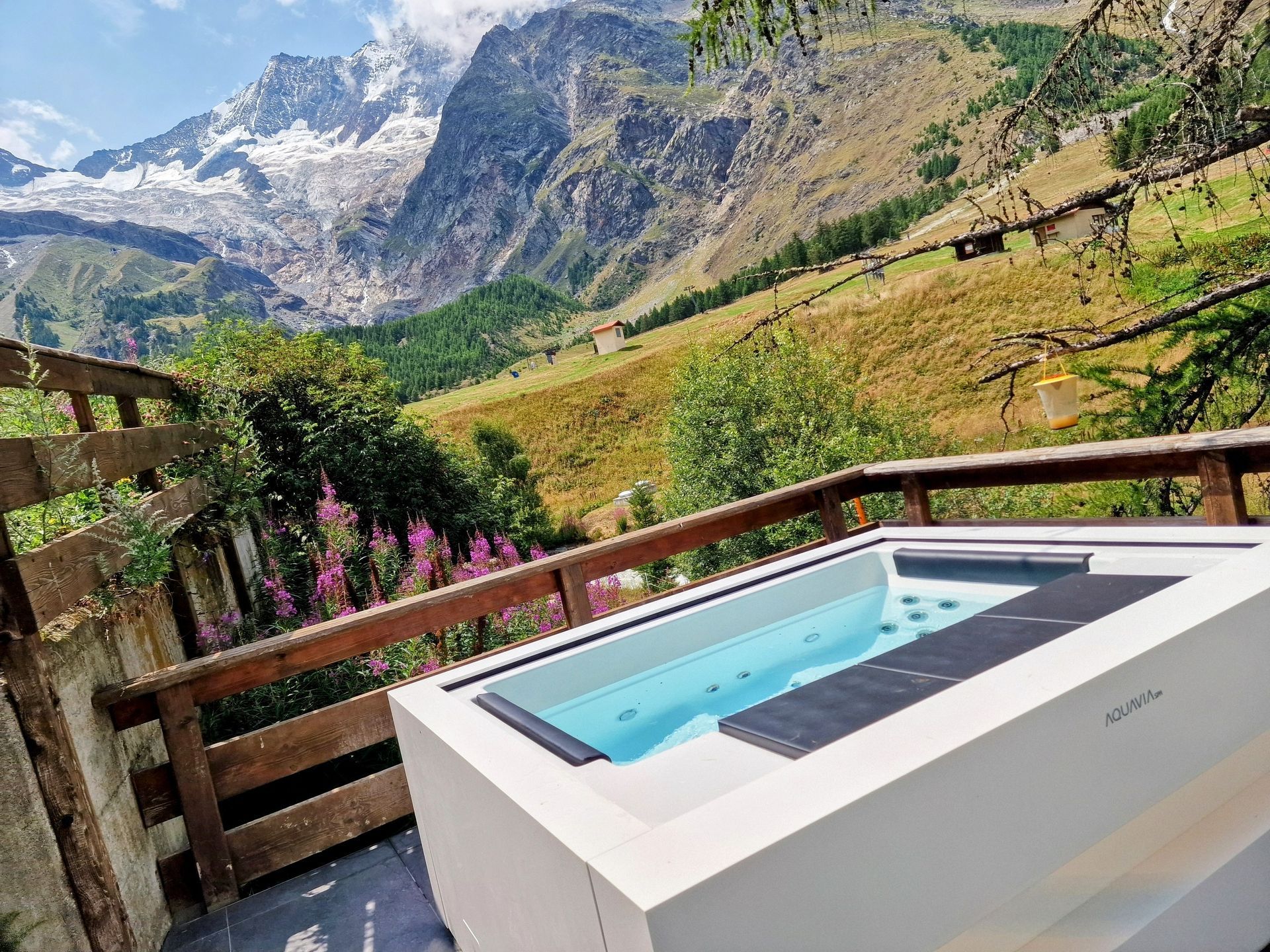 Hot tub on a mountain deck overlooking a green valley and snowy peaks