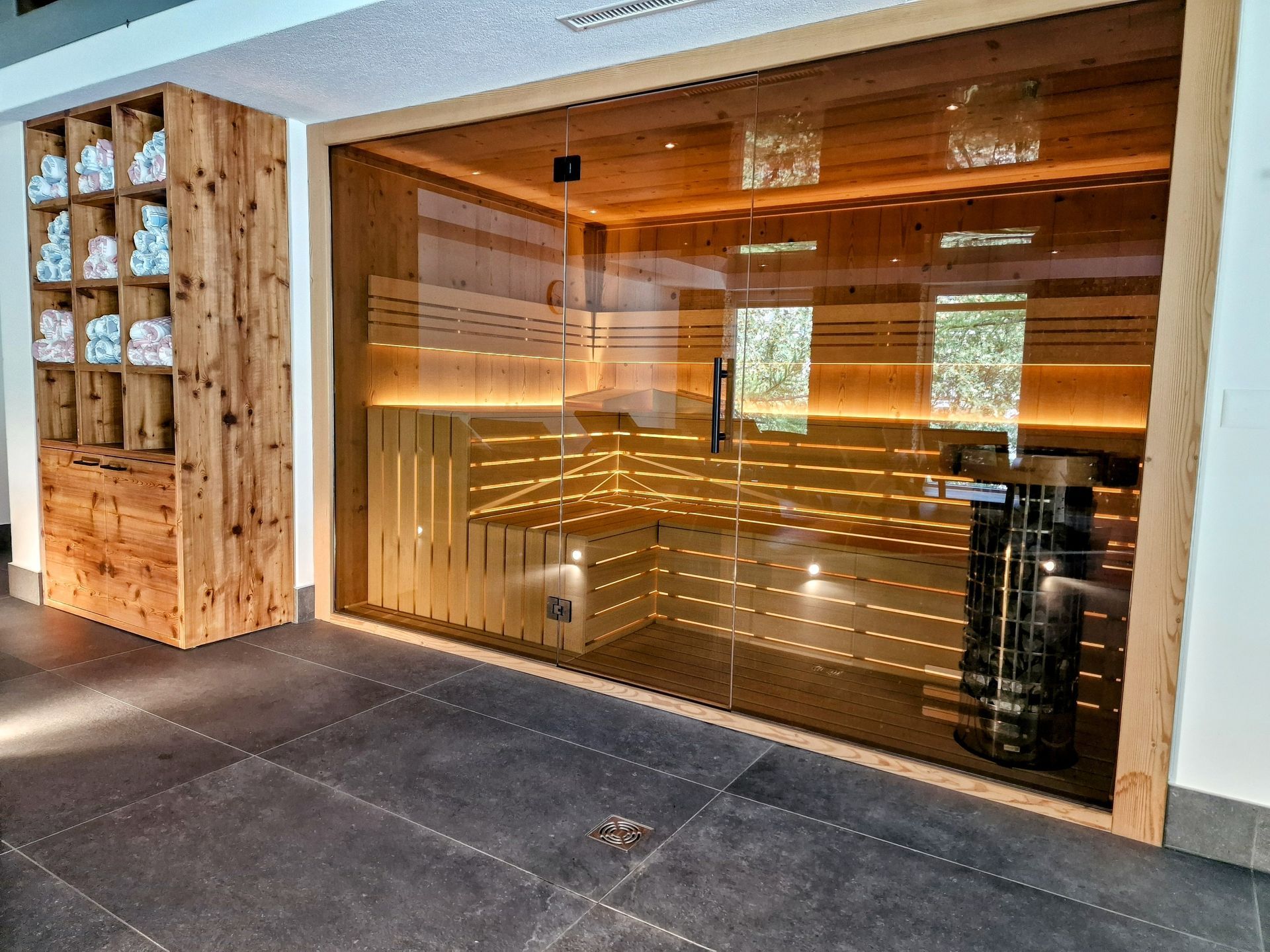 Wood-paneled sauna entrance with large glass door and warm interior lighting