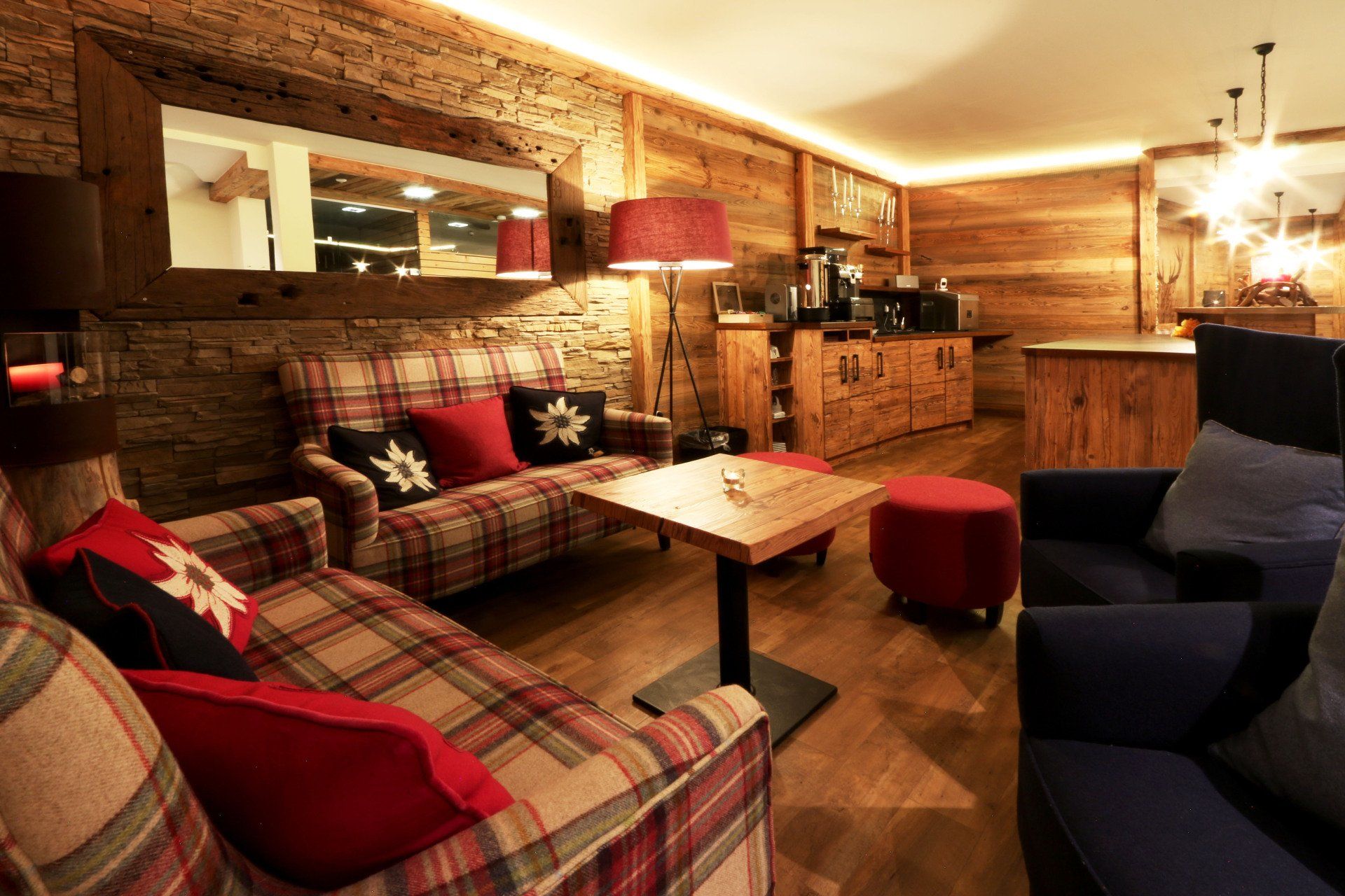 Cozy rustic lounge with plaid sofas, red lamps, wooden walls, and a small coffee table