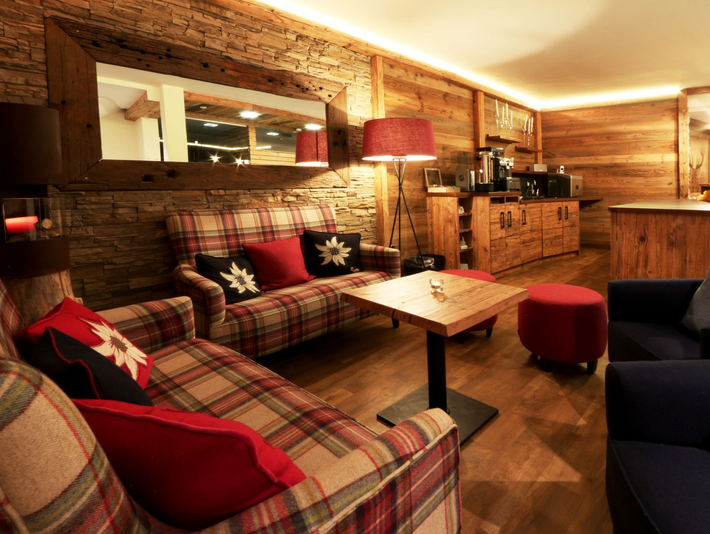 Cozy rustic lounge with plaid sofas, red lamps, wooden walls, and a small coffee table.
