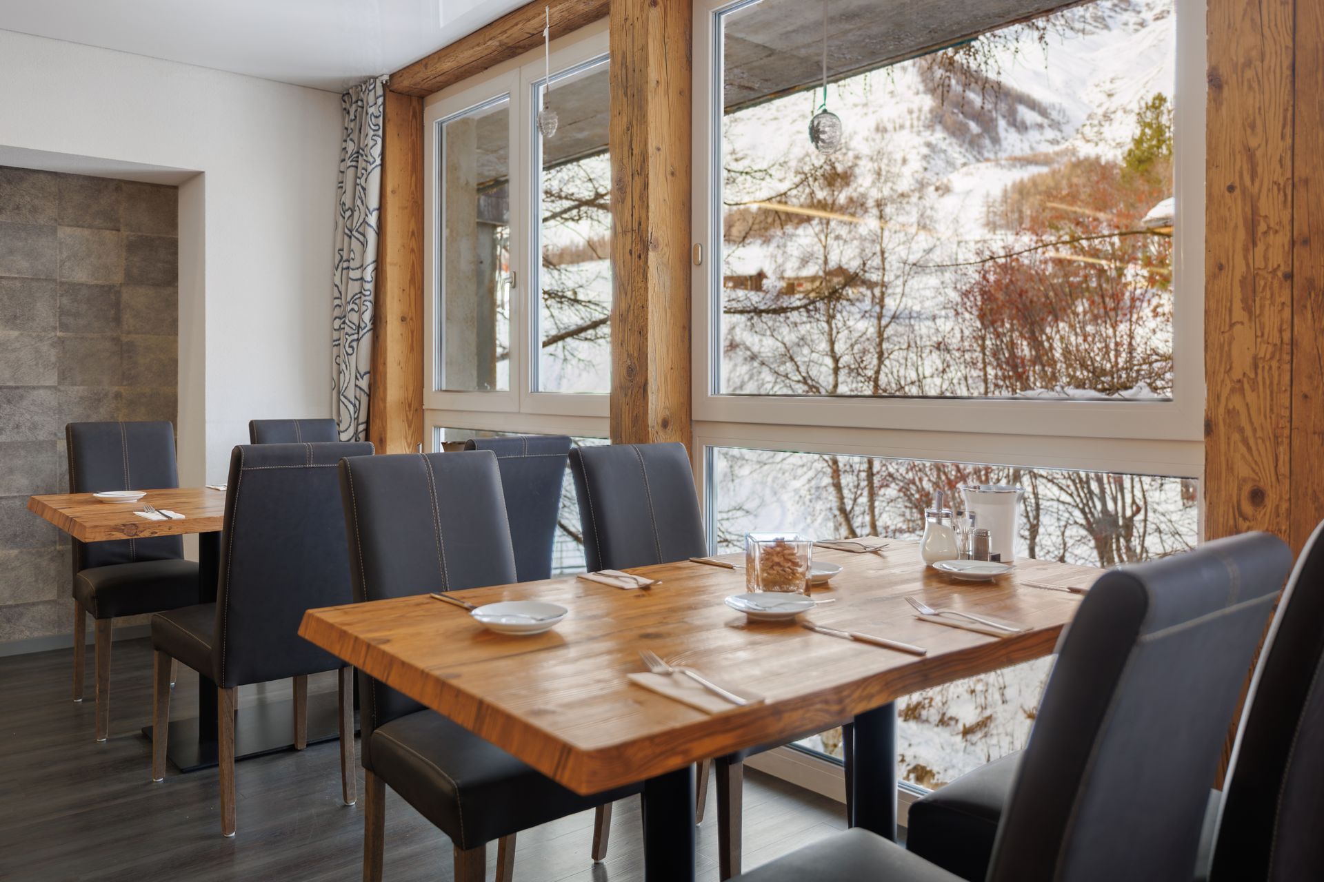 Modern dining area with wooden table, dark chairs, and large windows overlooking snowy trees