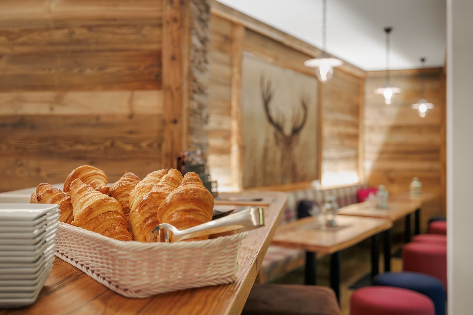 Pastries in a basket on a wooden table in a cozy café with booths and hanging lights