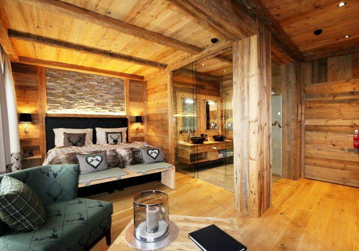 Cozy rustic log cabin bedroom with wood walls, stone fireplace, and green armchair