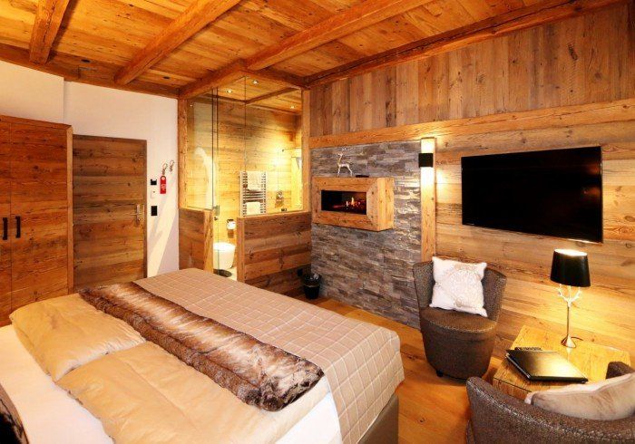 Rustic hotel bedroom with wooden ceiling, stone fireplace, bed, and warm lamp lighting