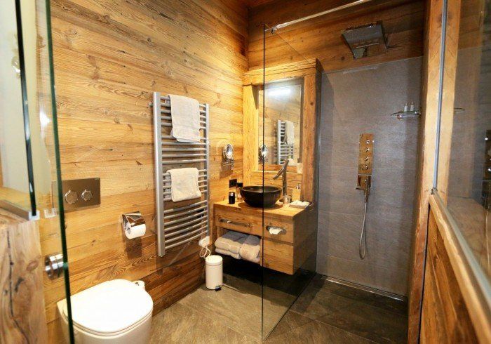 Wood-paneled modern bathroom with glass shower, sink, towel rack, and toilet