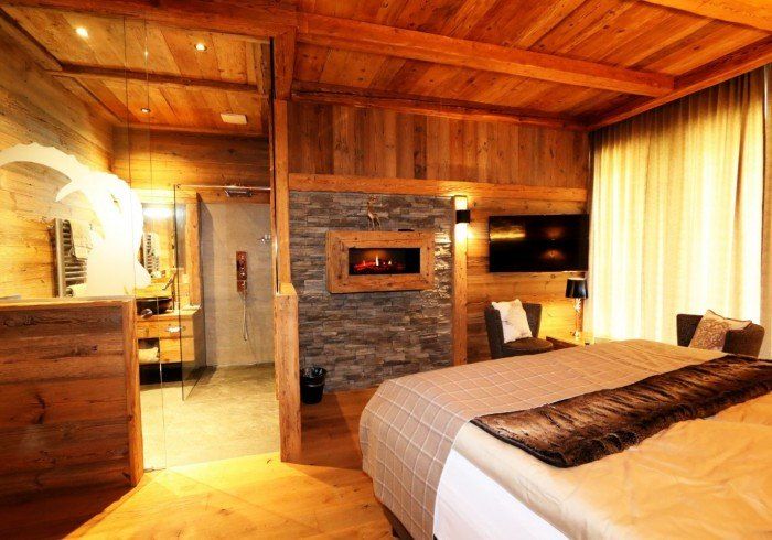 Cozy wood-paneled bedroom with stone fireplace, bed, and warm lighting
