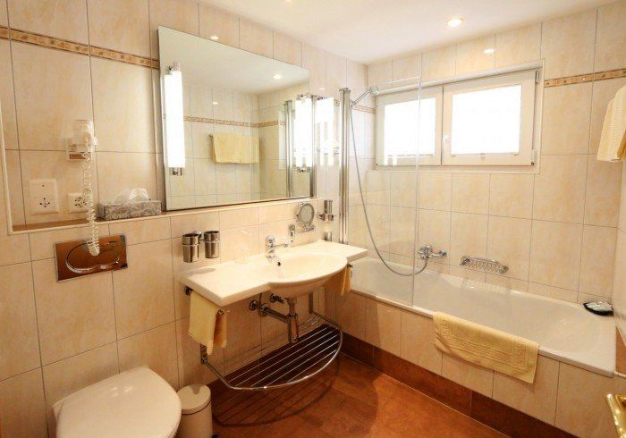 Bright beige bathroom with sink, mirror, toilet, bathtub, and window