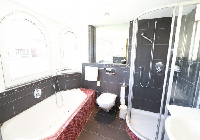 Bright bathroom with white tub, black tile shower, and glass shower enclosure