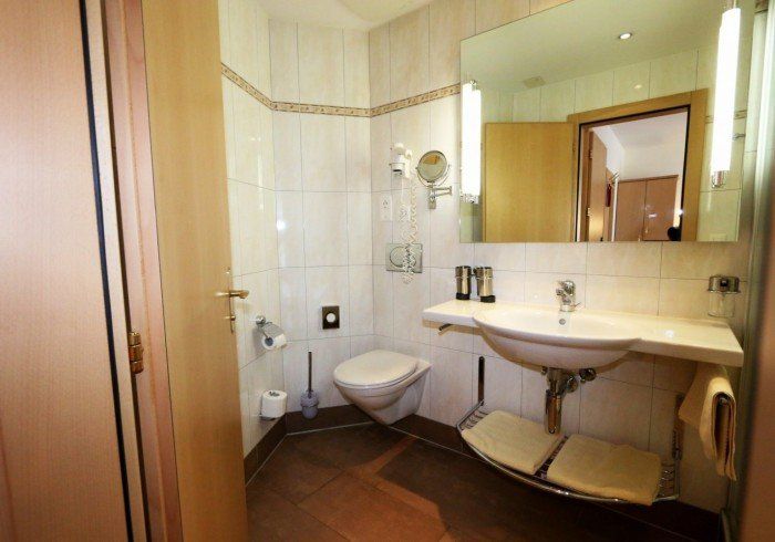 Small beige bathroom with toilet, sink, large mirror, and wooden door from overhead view