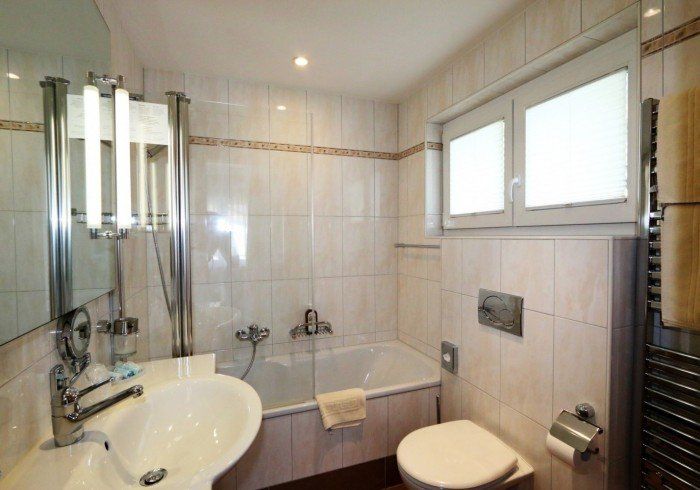 Bright white bathroom with shower, sink, toilet, and bathtub, lit by a window and ceiling lights.