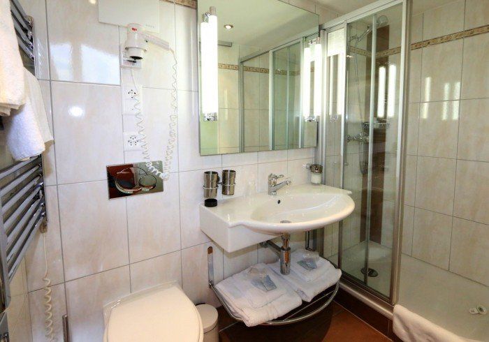 Compact bathroom with sink, shower enclosure, toilet, and beige tile walls
