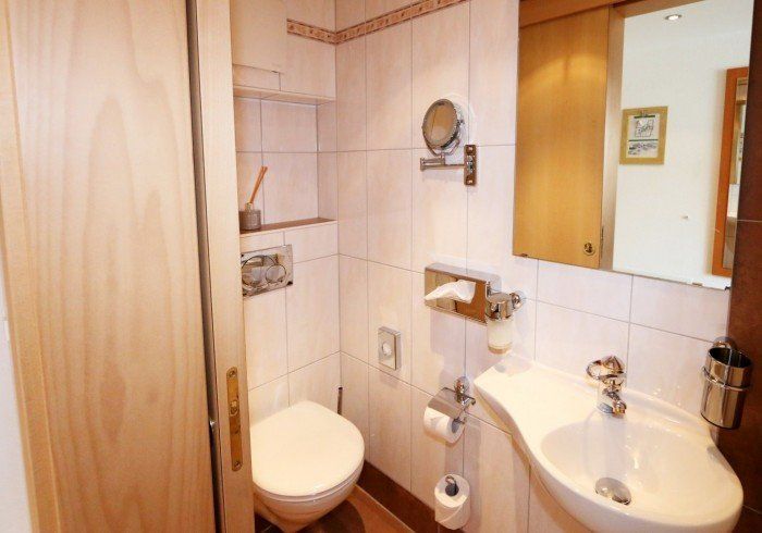 Small tiled bathroom with toilet, sink, mirror cabinet, and wooden storage cabinet