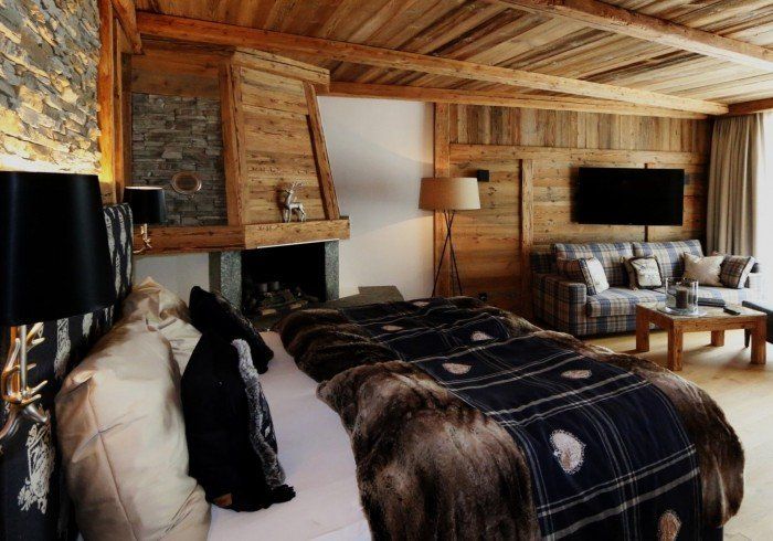 Rustic cabin bedroom with wood walls, plaid bedding, fireplace, and wall-mounted TV