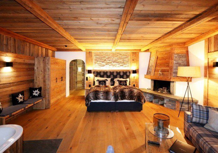 Cozy wood-paneled bedroom with king bed, stone fireplace, and warm lighting