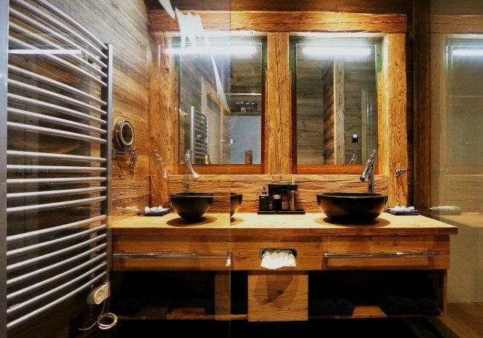Modern bathroom vanity with two black sinks, large mirror, and chrome towel rack, in warm wood tones
