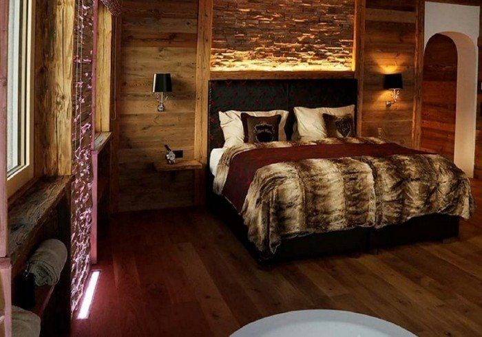 Cozy wood-paneled bedroom with a large bed, fur throw, and warm ambient lighting