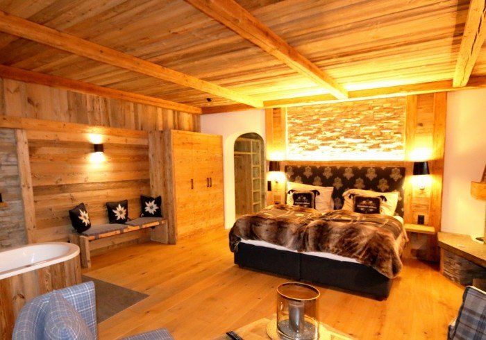 Warm wooden bedroom with a large bed, stone fireplace, and hot tub in a cozy cabin interior