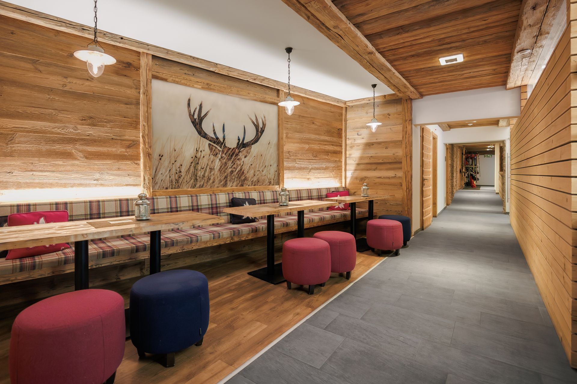 Rustic lodge hallway with wooden walls, antler wall art, cushioned benches, and a gray carpet runner