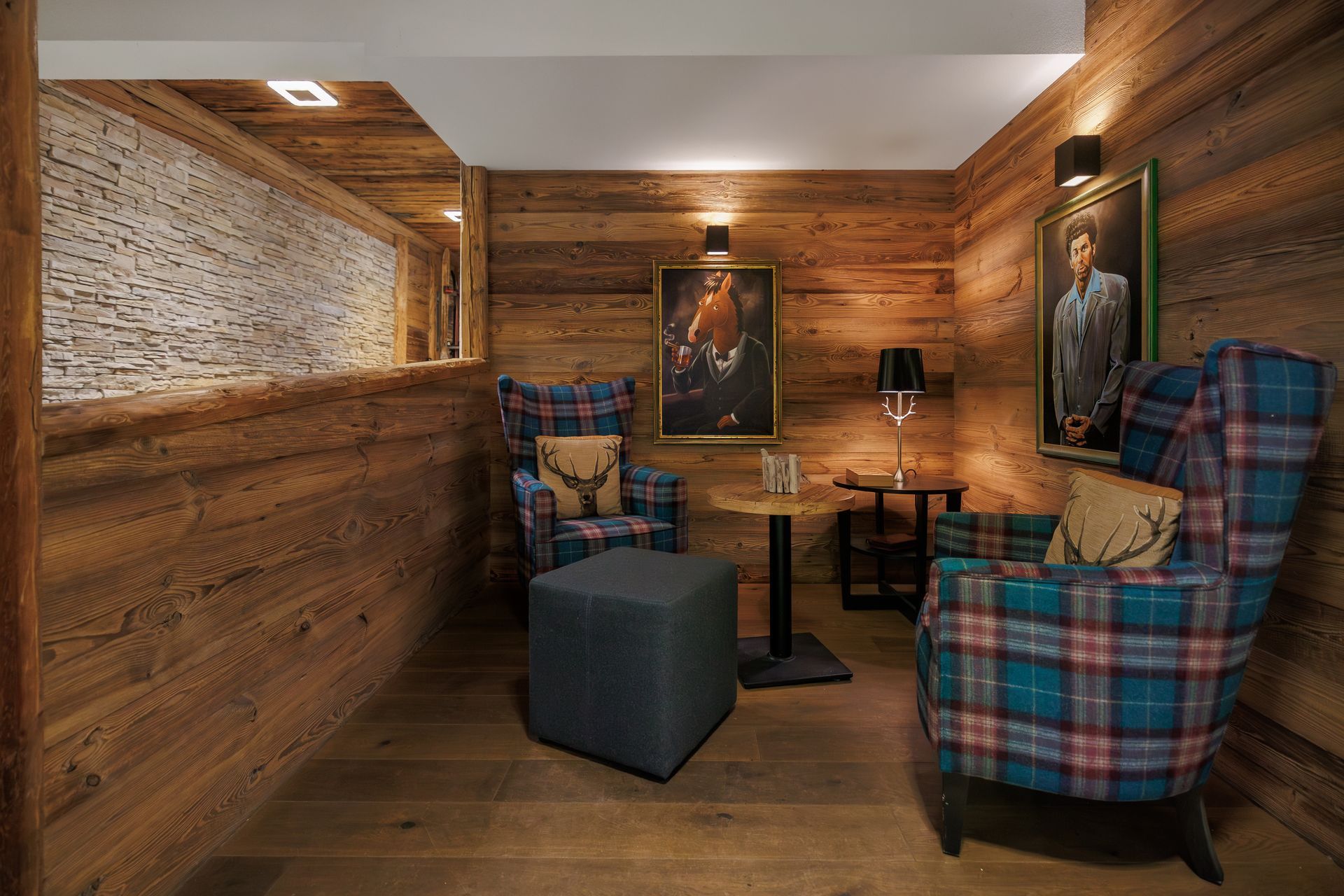 Cozy wood-paneled room with plaid armchairs, ottoman, lamp, and framed artwork.