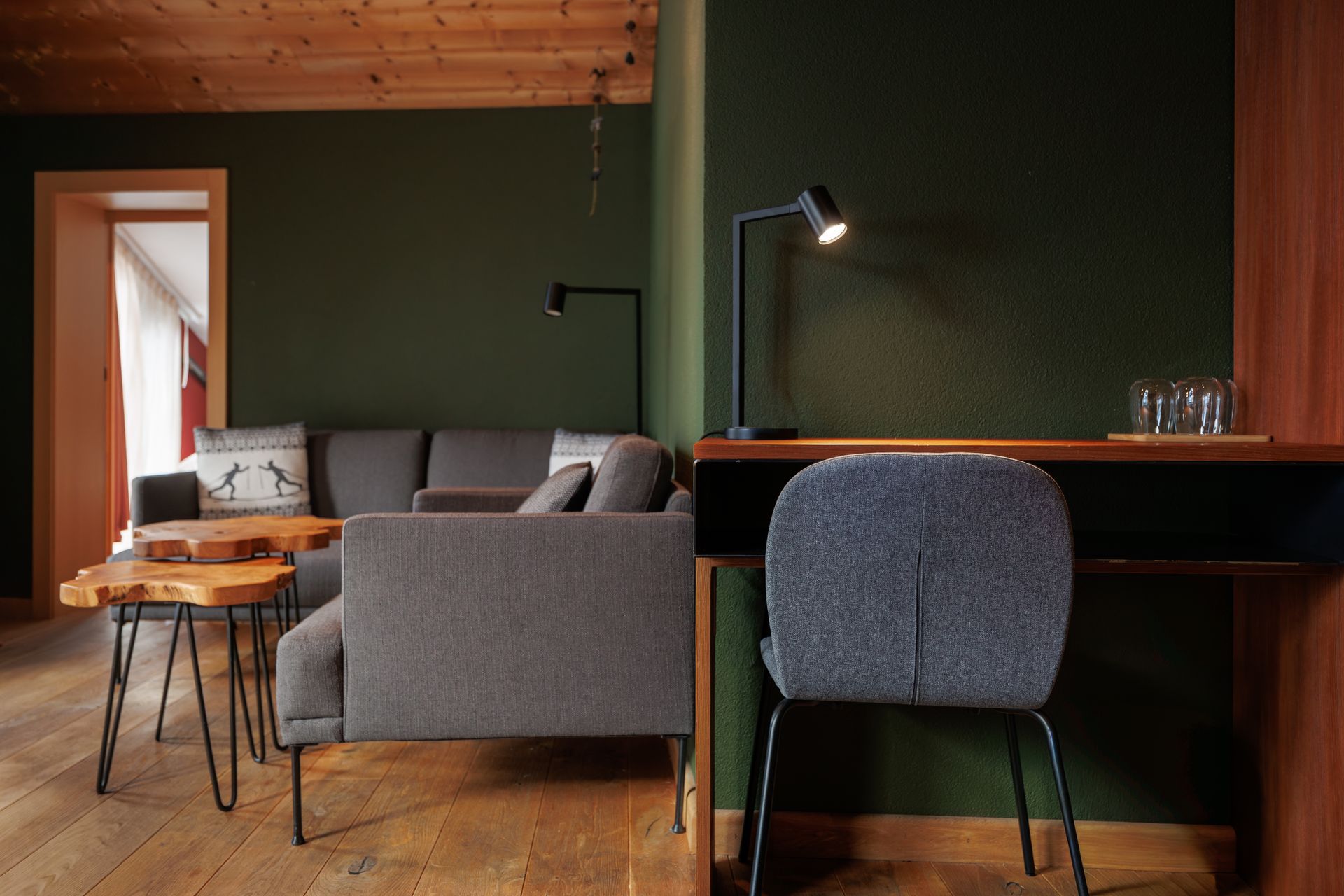 Modern living room with gray sofa, green wall, wooden table, and desk chair by a window