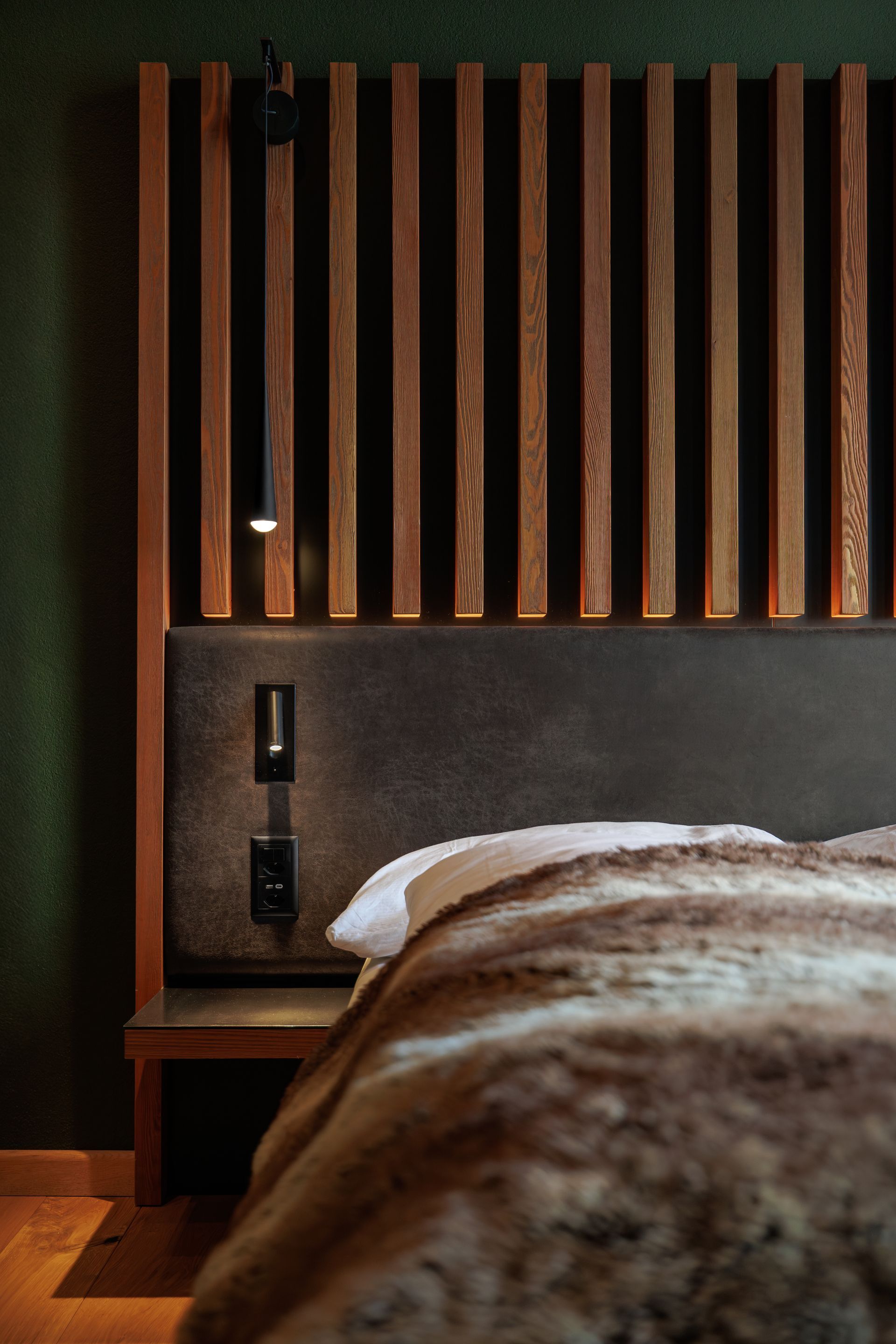 Modern bedroom with wood slat headboard, bedside shelf, and fur-covered bed.