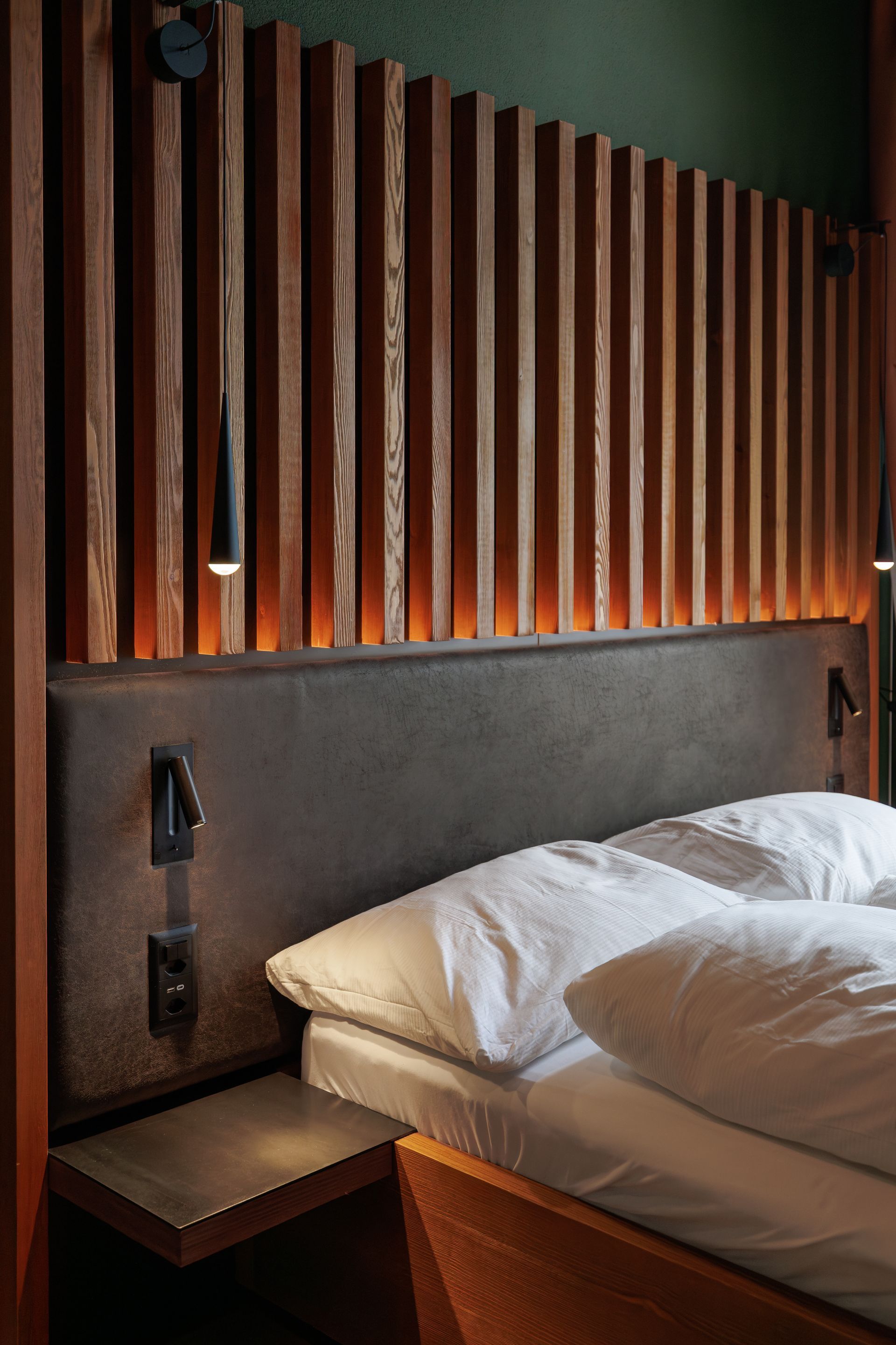 Modern bedroom with a bed, dark upholstered headboard, wood slat wall, and warm bedside lighting