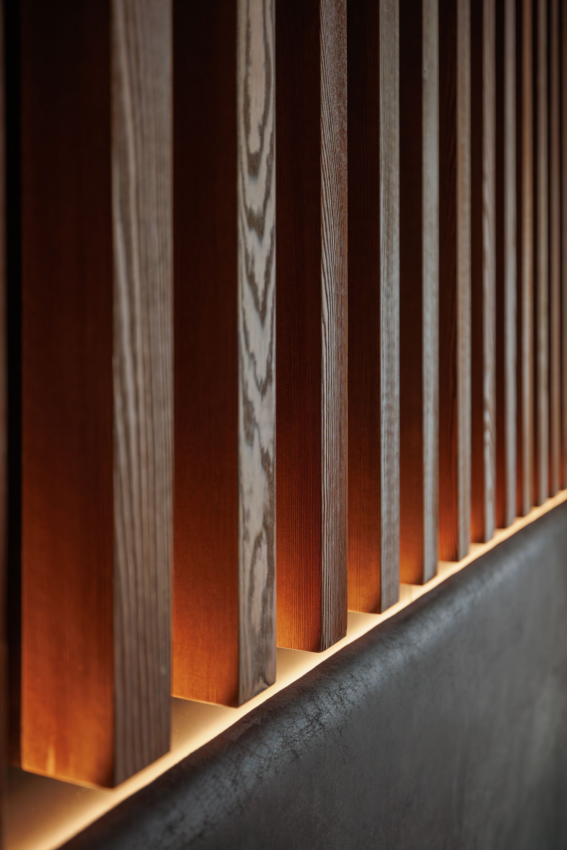 Close-up of vertical wooden slats above a dark ledge, lit by warm light.