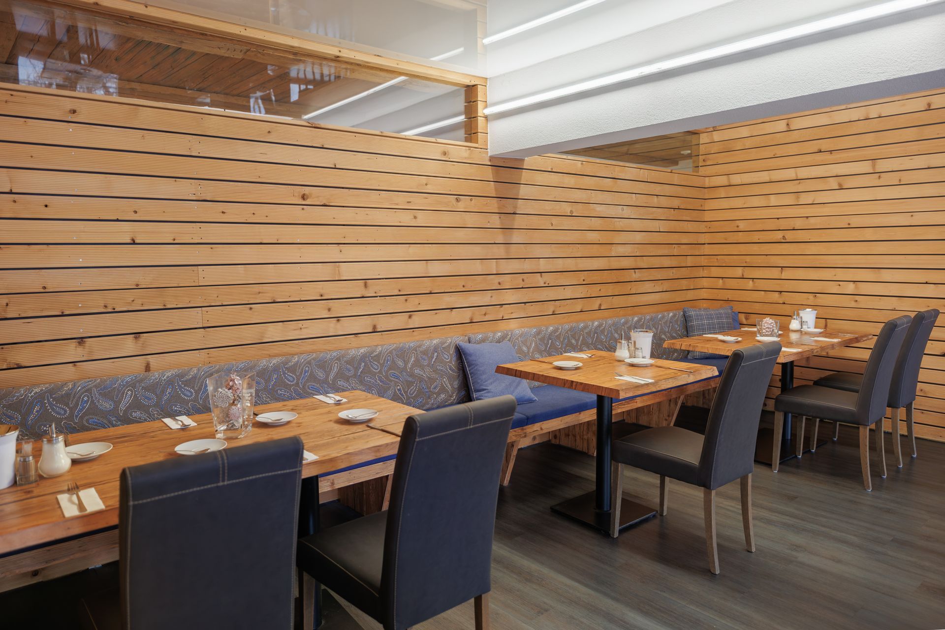 Empty modern restaurant with wooden slat walls, blue chairs, and set dining tables.