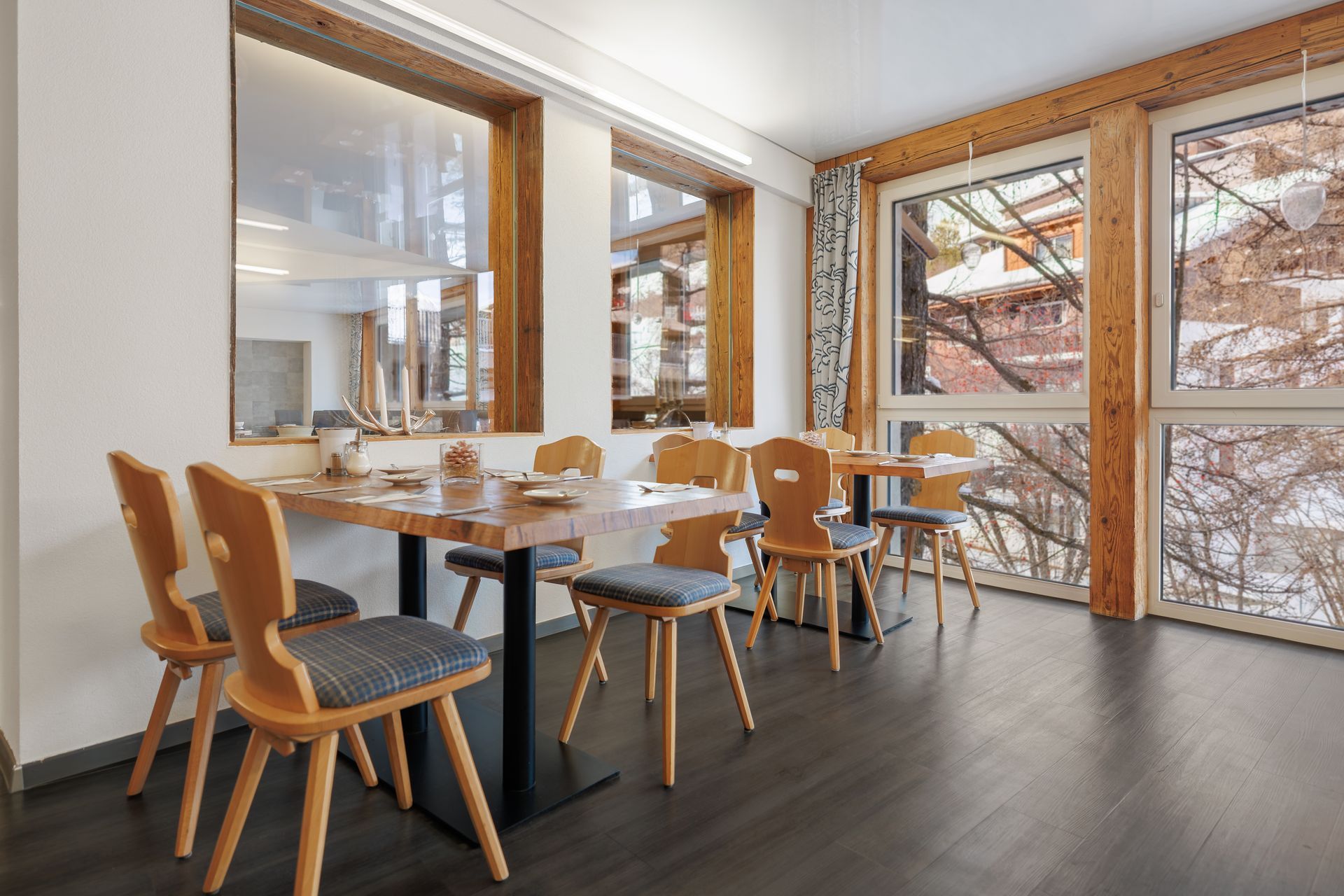 Modern dining room with wooden chairs, set table, large windows, and dark wood floors
