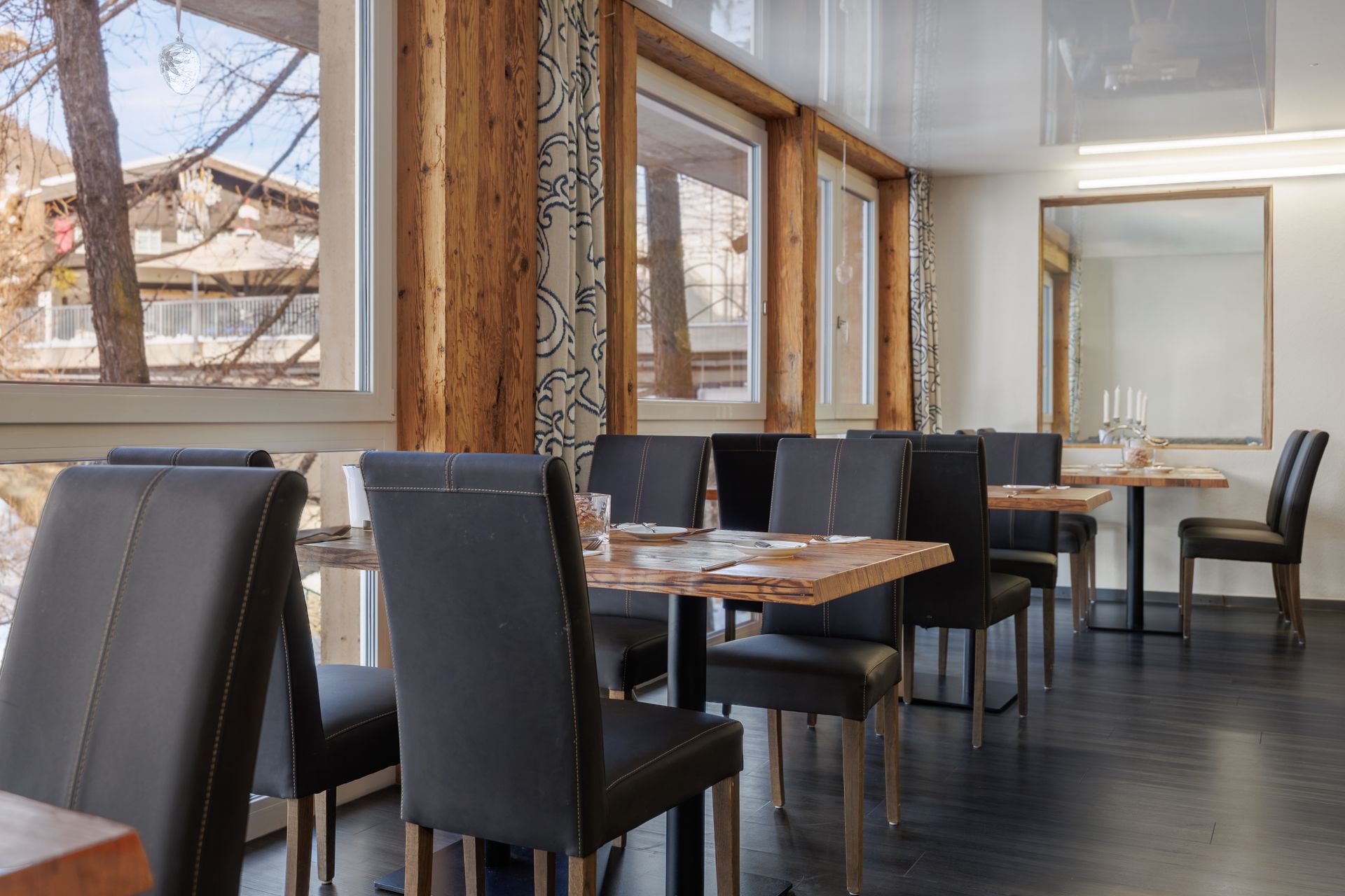 Modern café interior with black chairs, wooden tables, and large windows overlooking a snowy street
