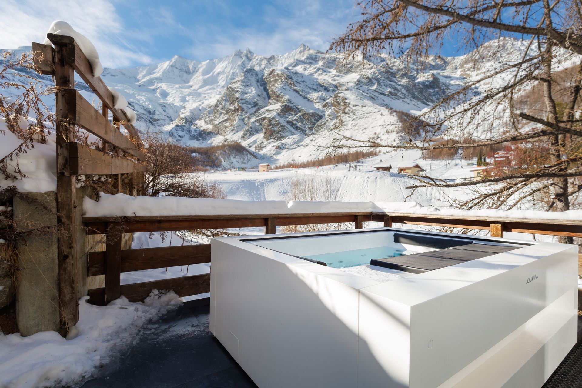 Snowy mountain view from a wooden deck with a white hot tub in the foreground